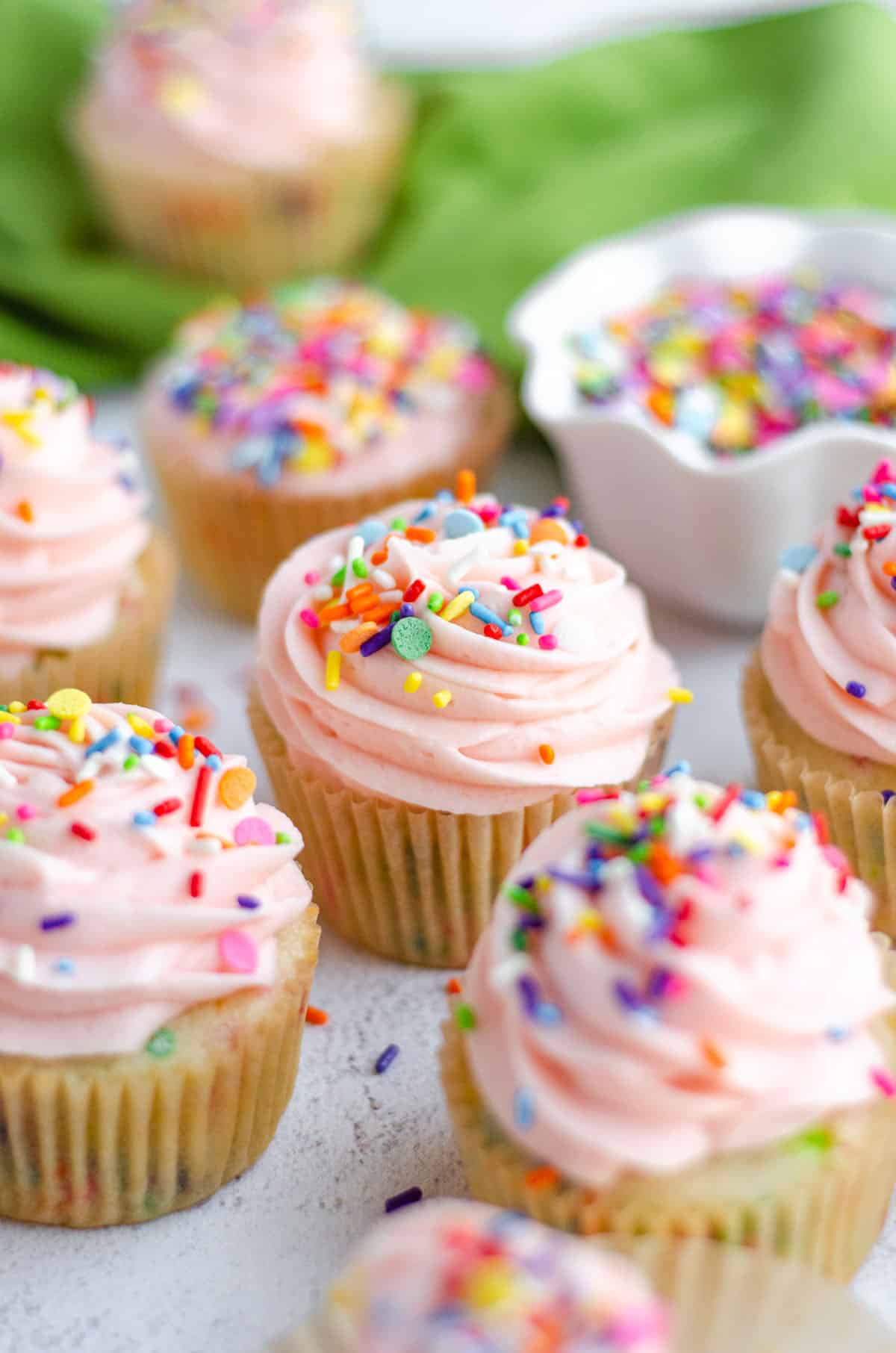 homemade funfetti cupcakes with pink frosting and a bowl of sprinkles in the background