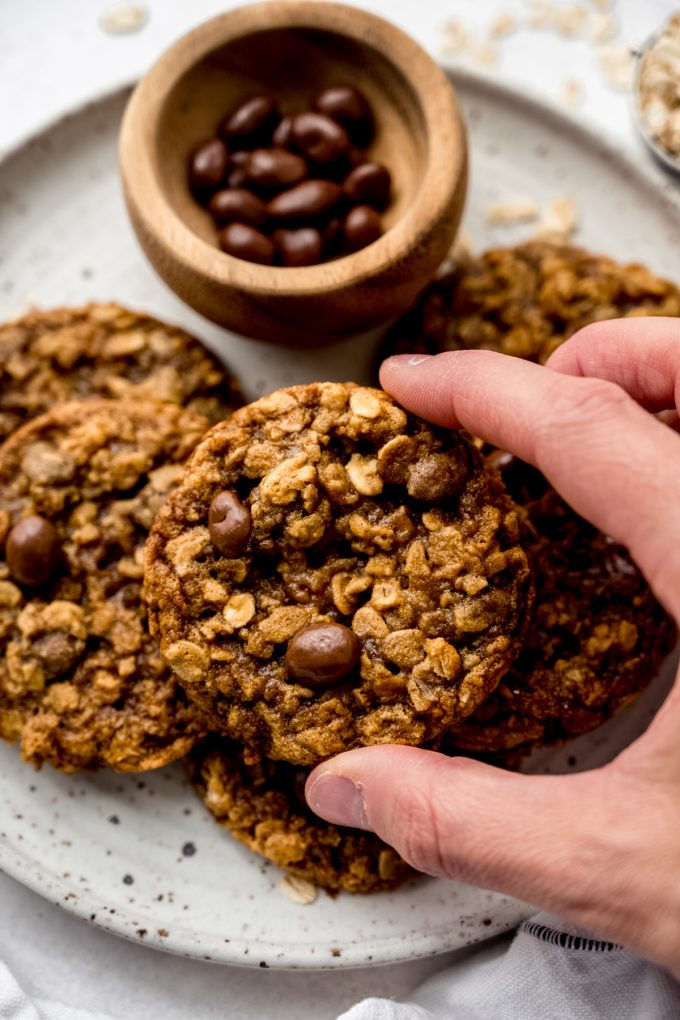 Aerial photo of someone holding one of the oatmeal Raisinet cookies that are on a plate.