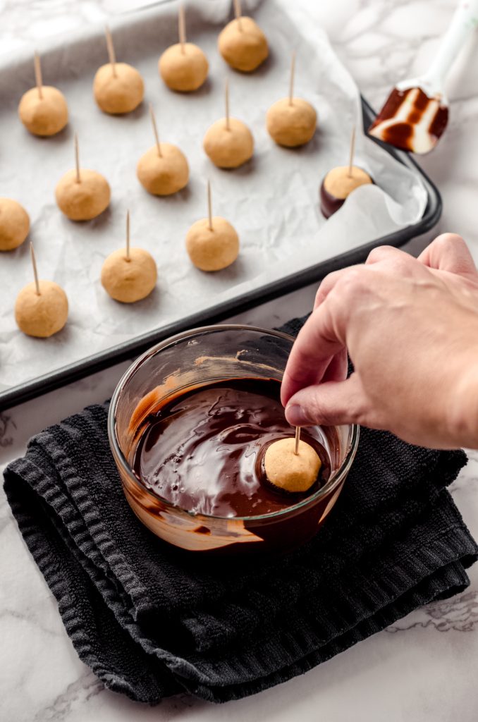 A hand dipping a peanut butter buckeye ball into chocolate.