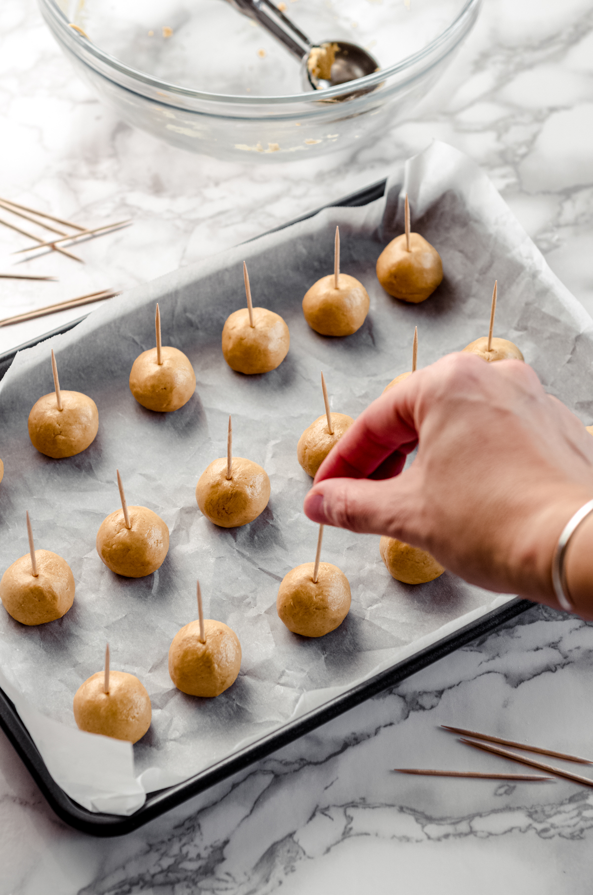 A hand pressing toothpicks into peanut butter balls to make buckeyes.