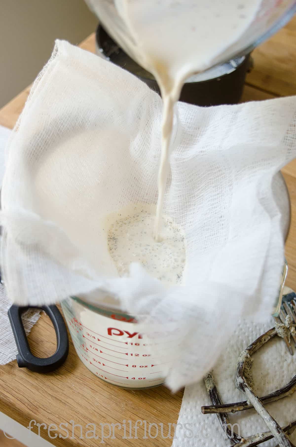 Straining vanilla bean infused cream through a mesh cloth to make homemade French vanilla coffee creamer.