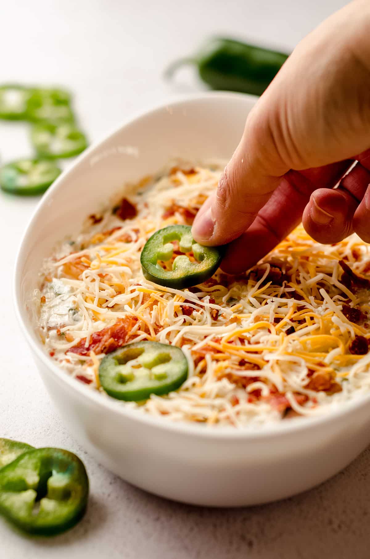 hand placing a slice of jalapeno pepper on top of jalapeno cream cheese dip before baking it