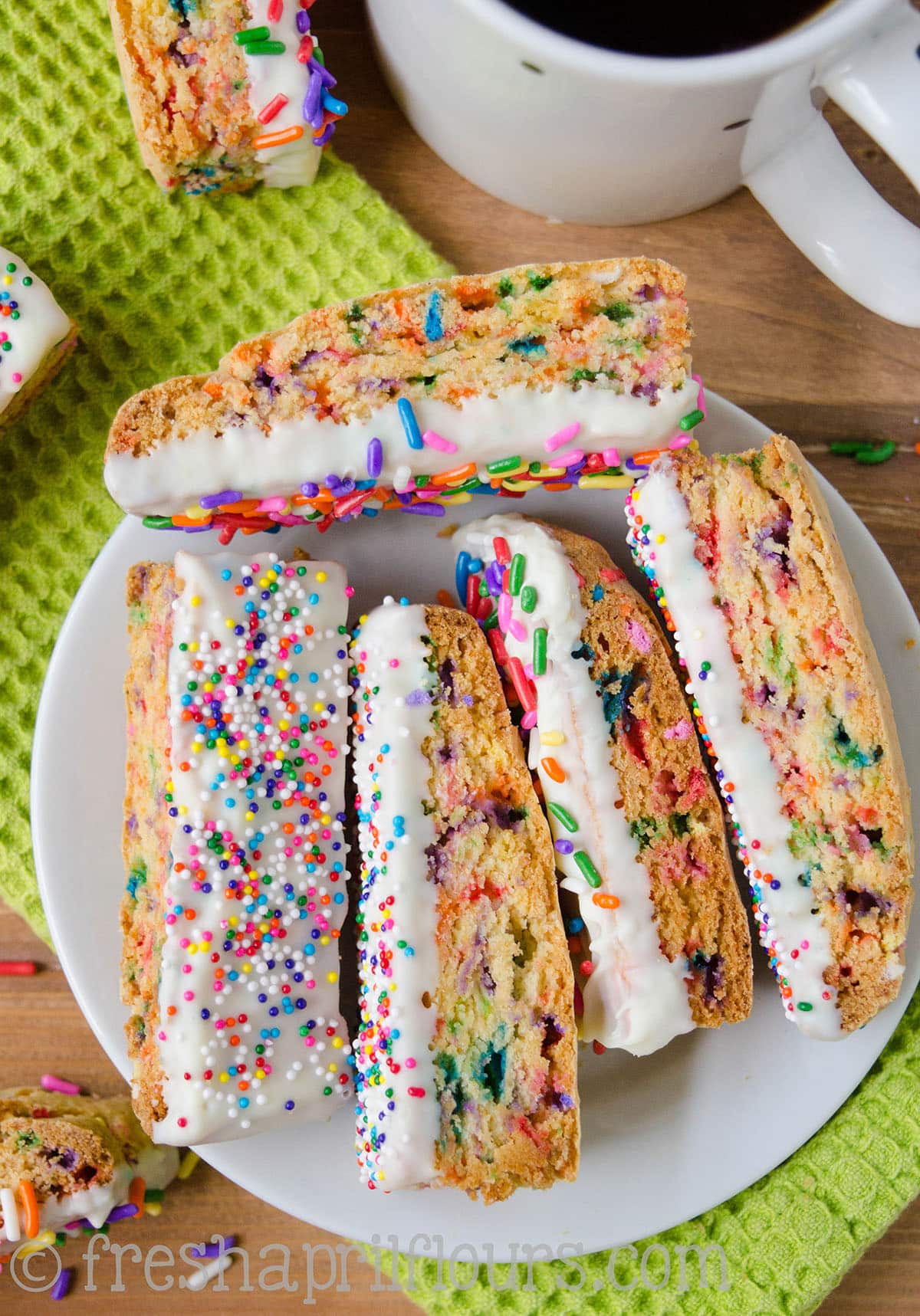 Funfetti biscotti on a plate with a cup of coffee in the background.