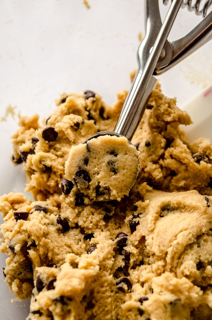 A bowl of mini chocolate chip cookie dough with a mini cookie scoop in it.