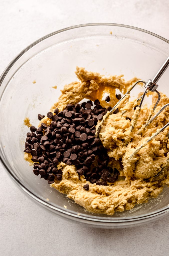 A bowl of mini chocolate chip cookie dough with beaters in it.