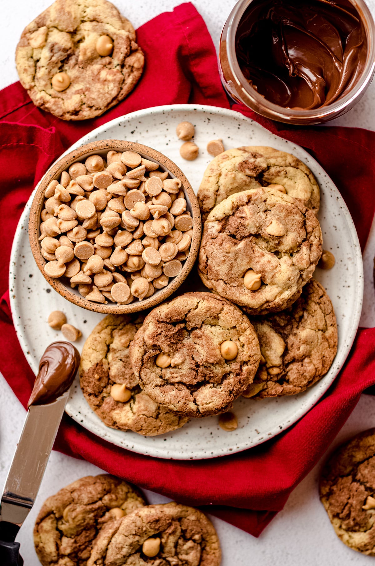 aerial photo of nutella peanut butter chip cookies on a plate with peanut butter chips and a spatula with nutella