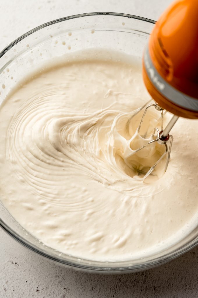 A bowl of the base ingredients for peanut butter ripple being whipped with a handheld mixer.