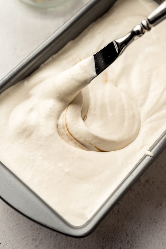 Someone is swirling peanut butter into the base of peanut butter ripple ice cream with a butter knife.