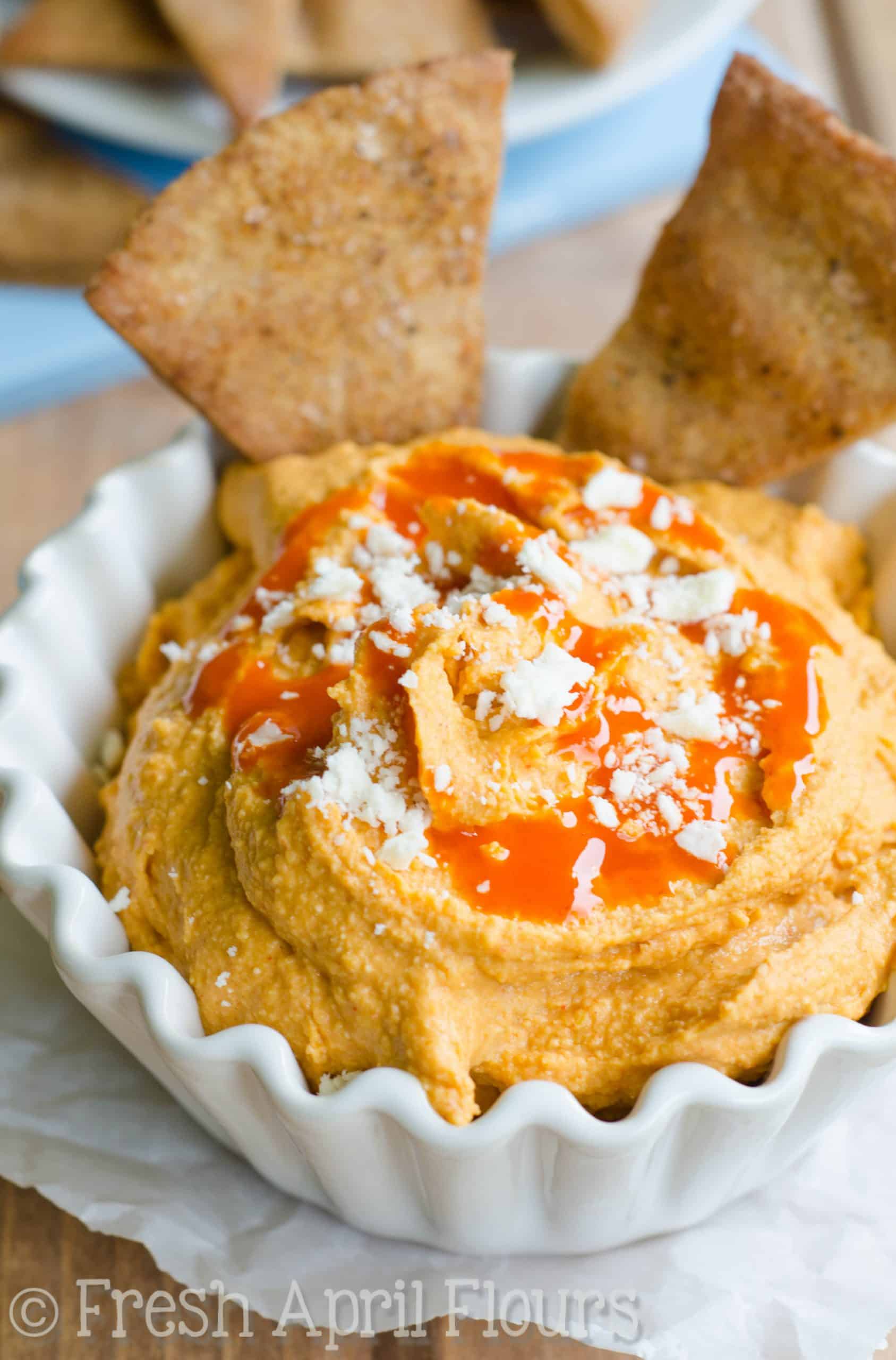 A bowl of creamy buffalo hummus on a piece of parchment paper.