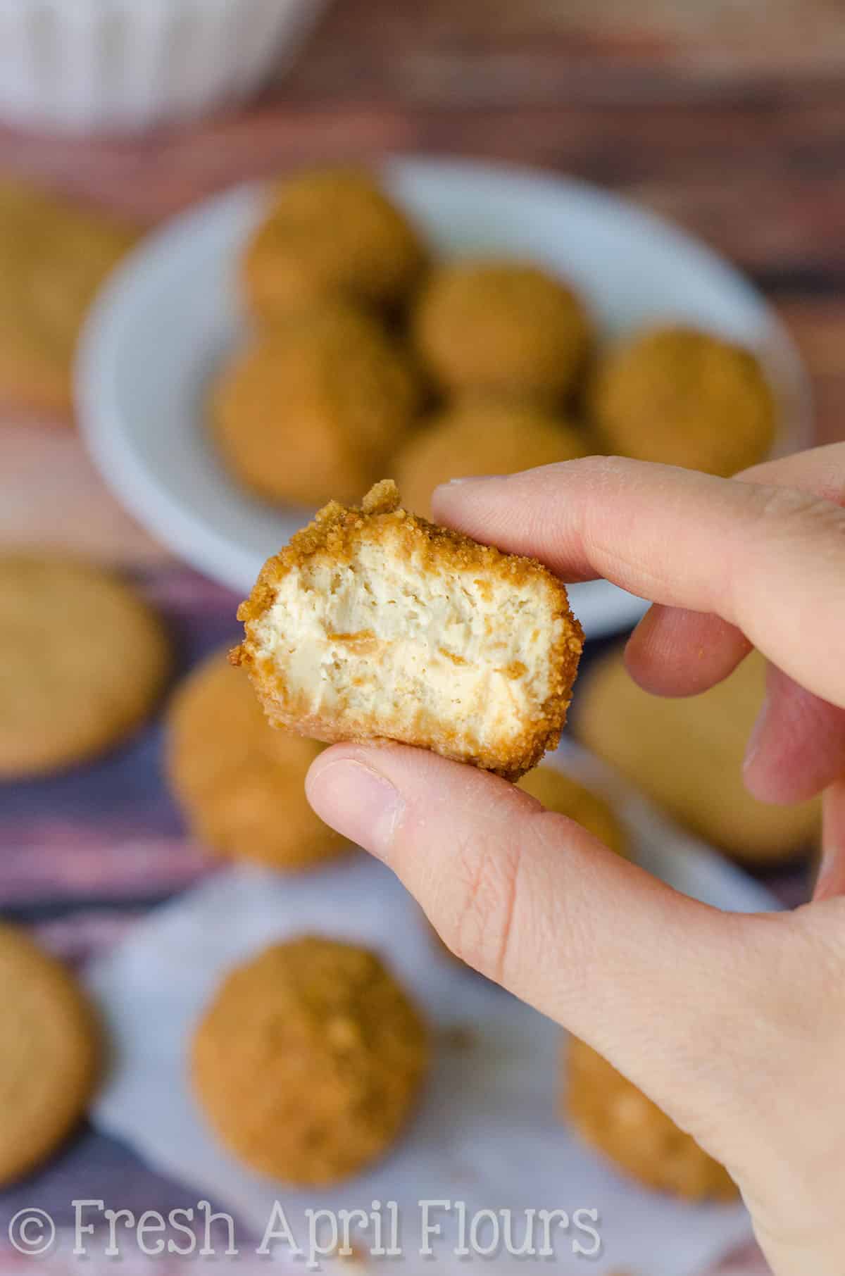 A gingersnap cheesecake bite with a bite taken out of it. Someone is holding it between their thumb and pointer finger.