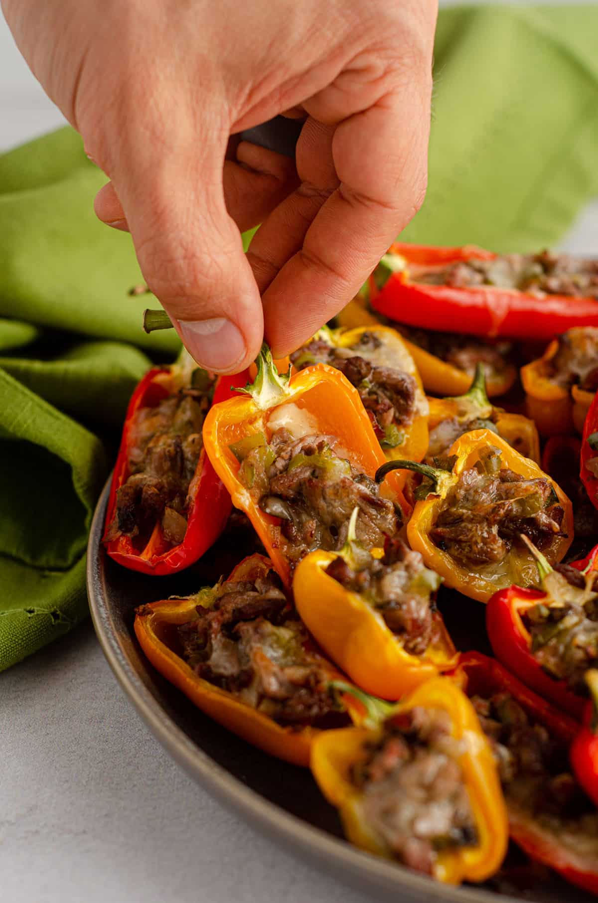 hand grabbing mini philly cheesesteak stuffed pepper off of a platter