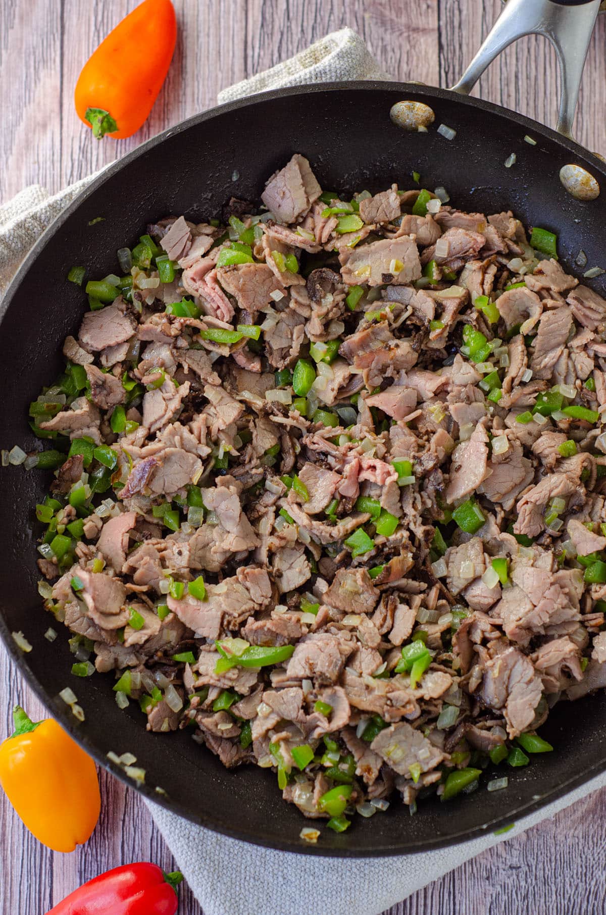 meat, peppers, mushrooms, and onions in a frying pan