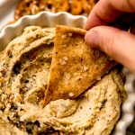 Someone is dipping a homemade pita chip into hummus.