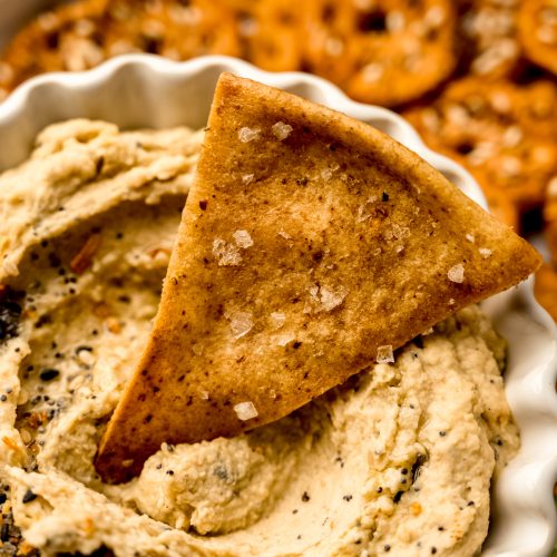A homemade pita chip in a bowl of hummus.