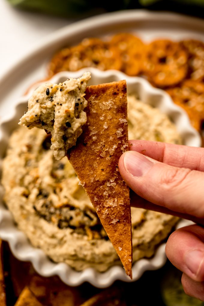 Someone is holding a homemade pita chip dipped into hummus.