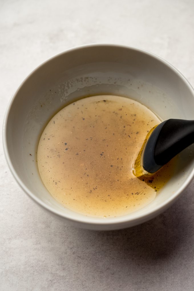 A bowl of seasoned oil with a pastry brush in it.