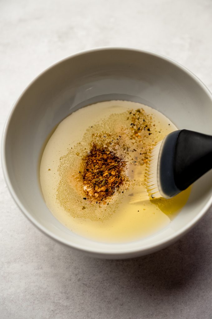 A bowl of seasoned oil with a pastry brush in it.