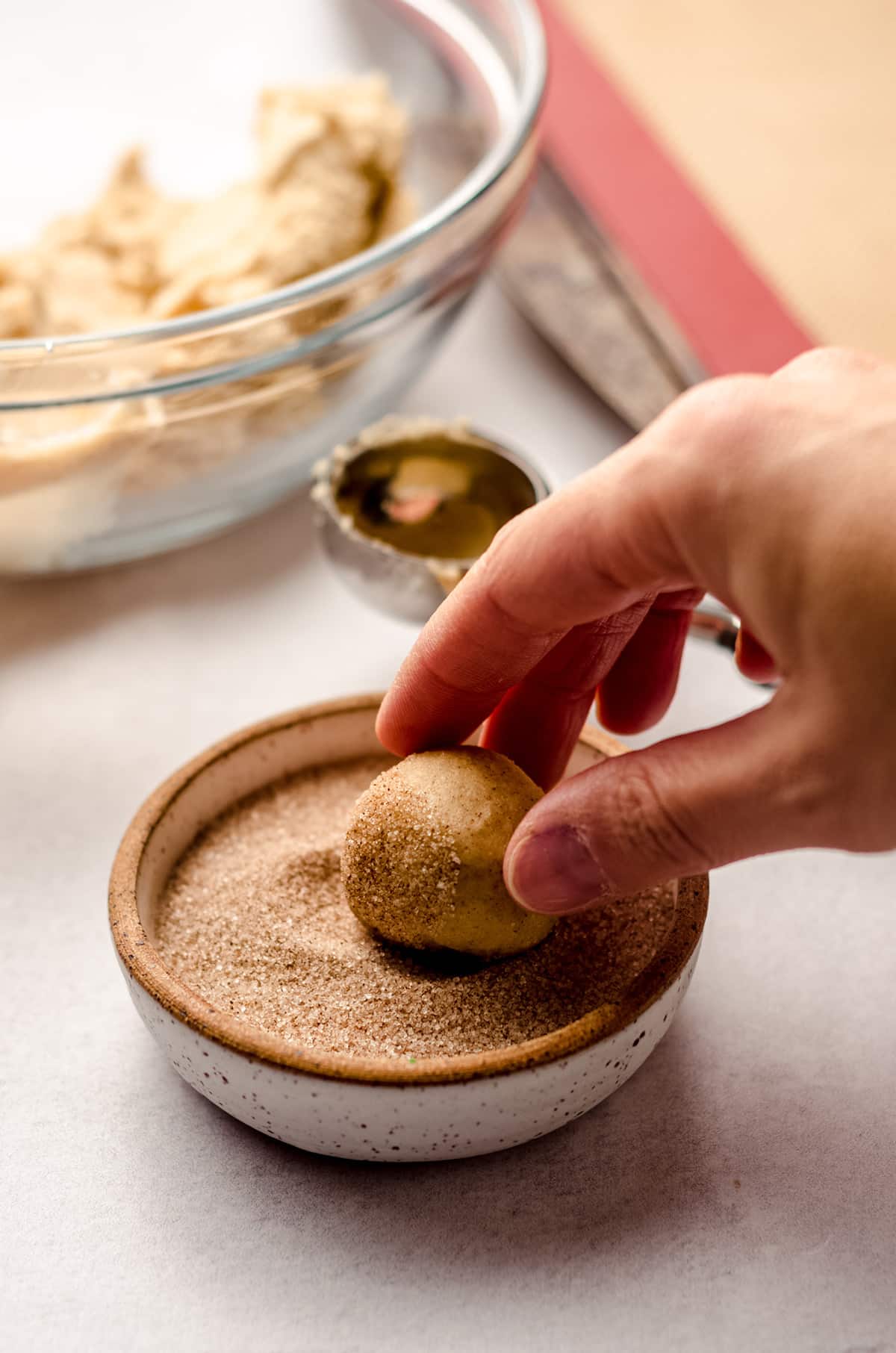 rolling snickerdoodle cookie dough in a bowl of cinnamon-sugar