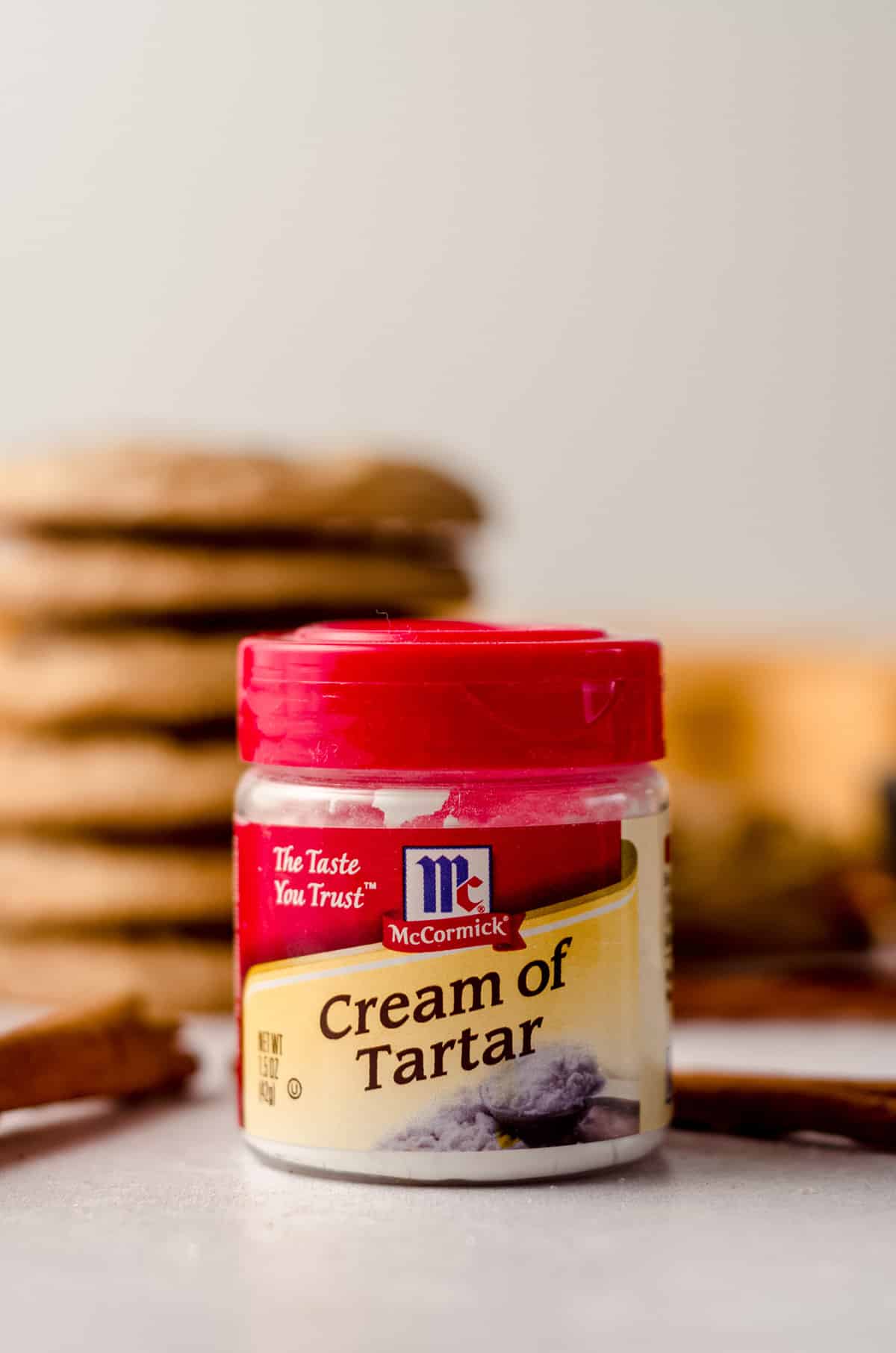 jar of cream of tartar with a stack of snickerdoodles behind it