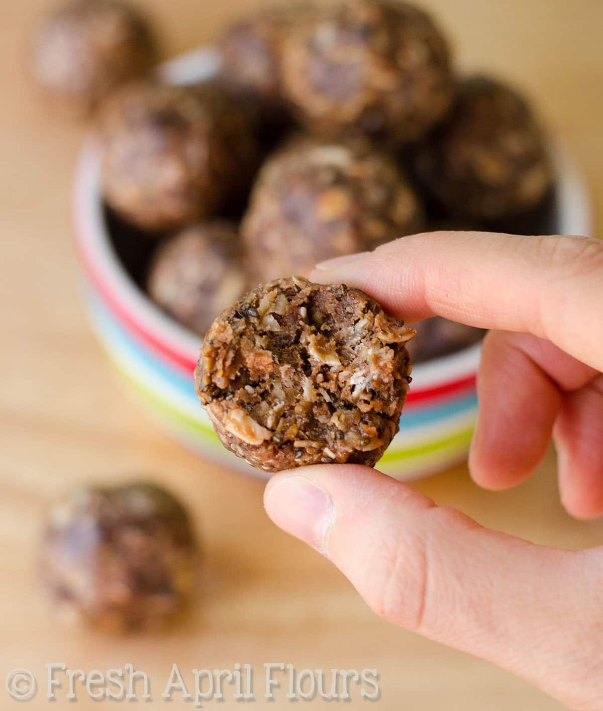 Fingers holding a chocolate chip oat bite that has a bite taken out of it.