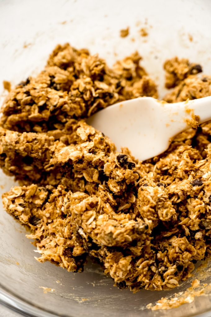 A bowl of the mixture for chocolate chip oat bites with a spatula in it.