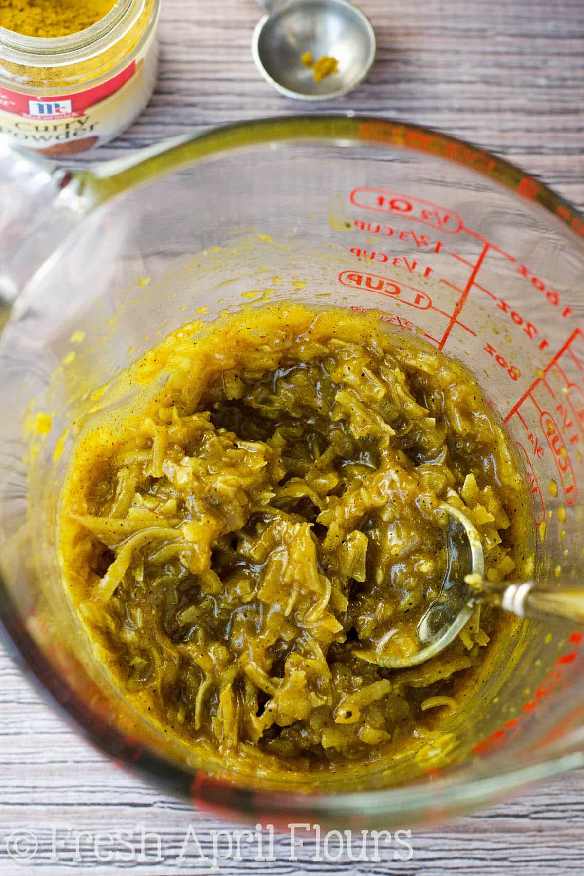 Mixture of coconut and curry for toasted coconut curry peanuts in a glass measuring cup with a spoon. 