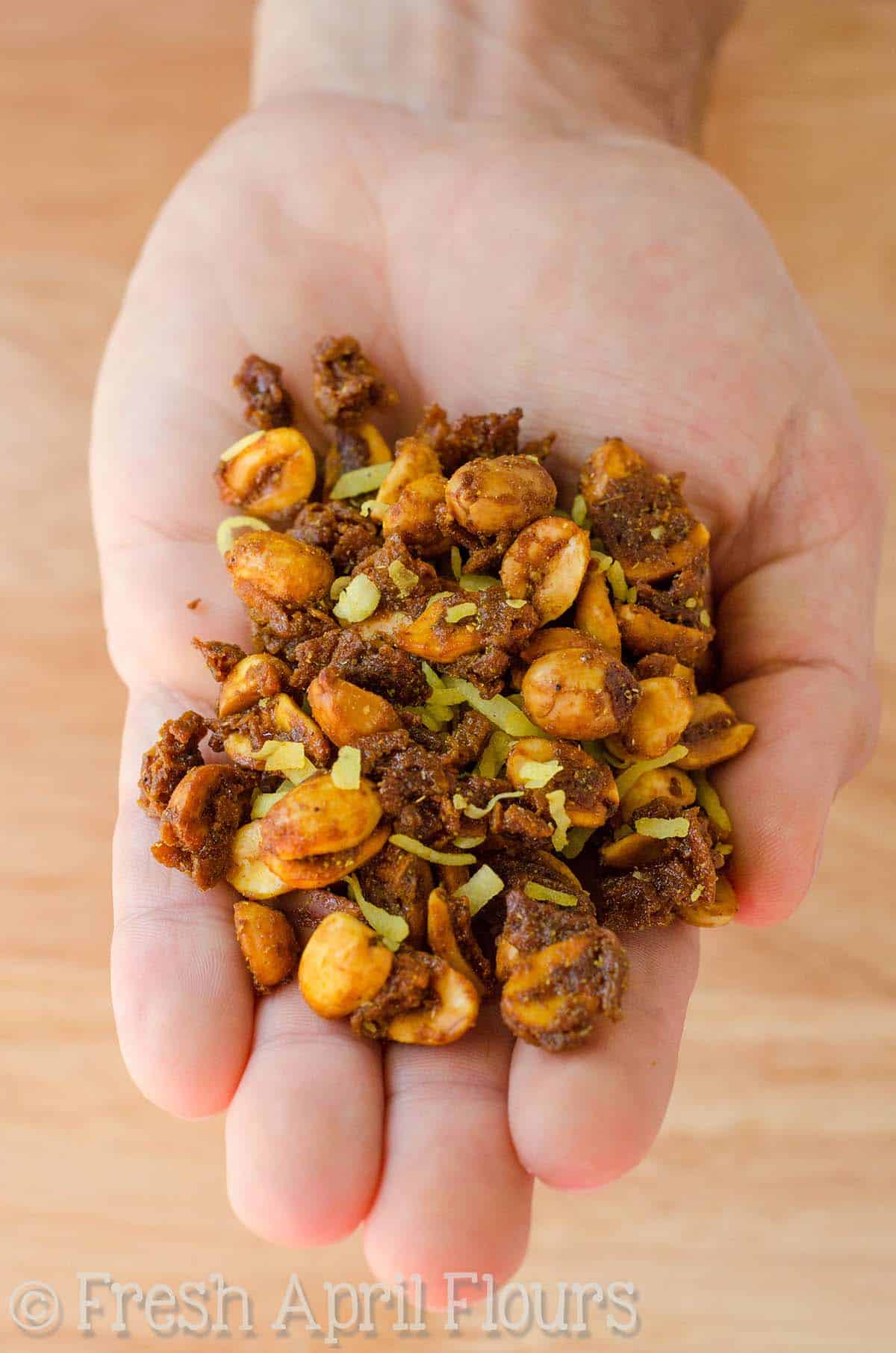 A hand holding toasted coconut curry peanuts.