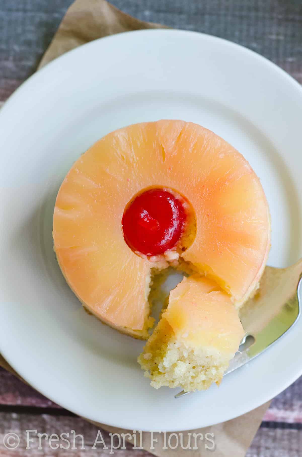 Aerial photo of a mini pineapple upside down cake on a plate with a forkful taken out of it.