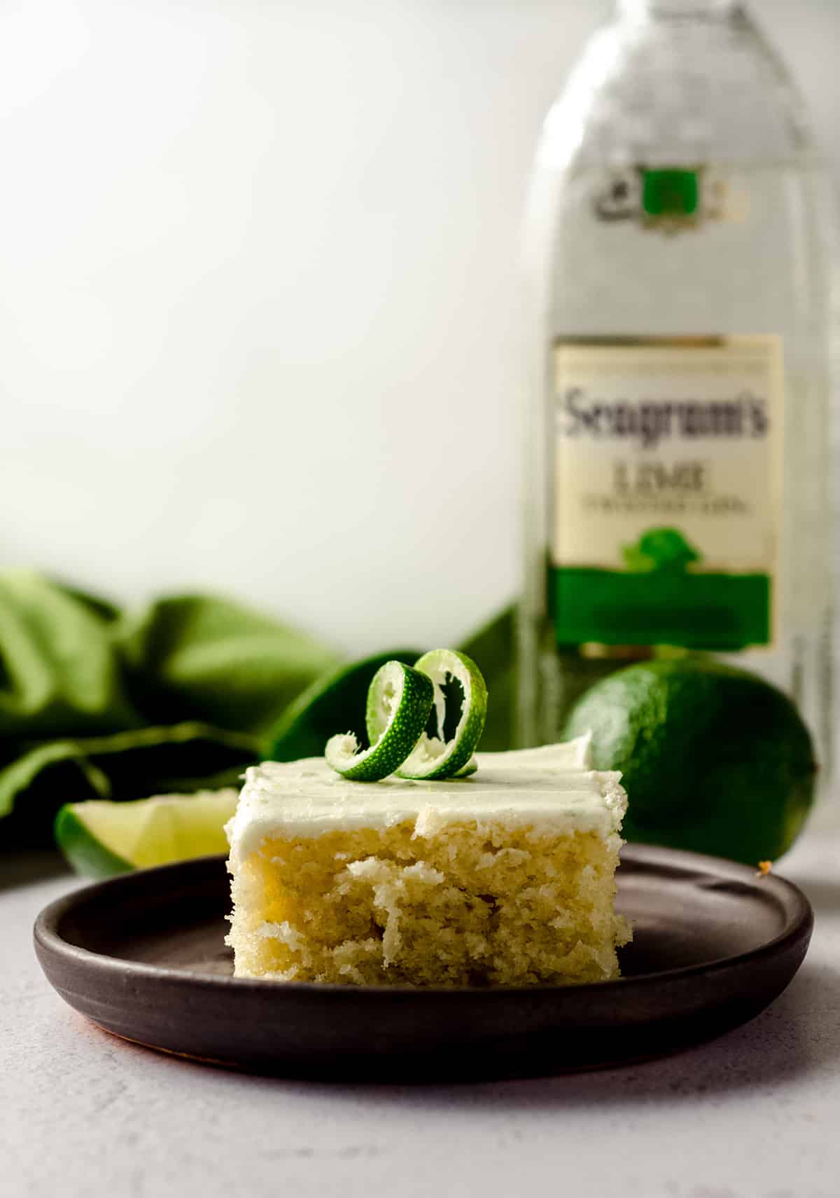 slice of gin and tonic cake sitting on a plate with a bottle of gin and limes in the background