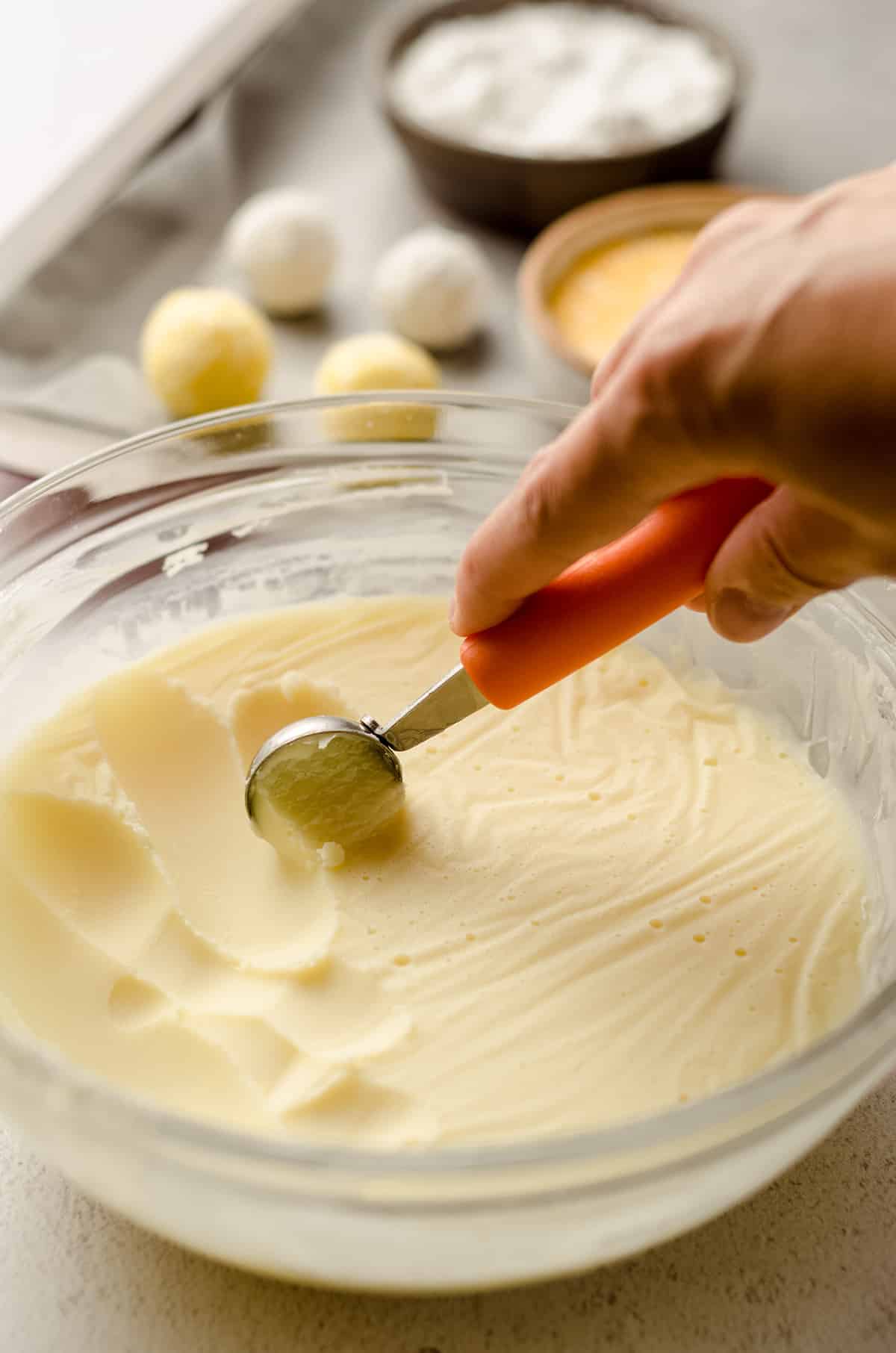 using a melon baller to scoop lemon ganache out of a bowl to make lemon truffles