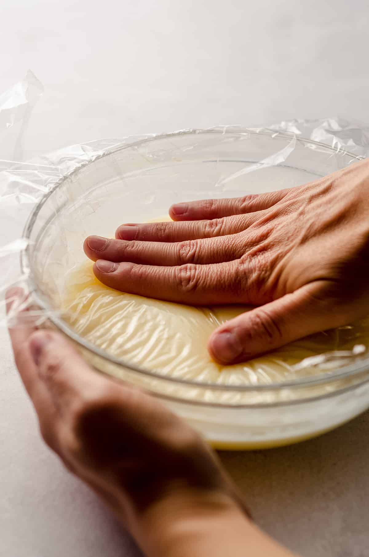 hand pressing plastic wrap onto a bowl of ganache to prevent it from forming a film