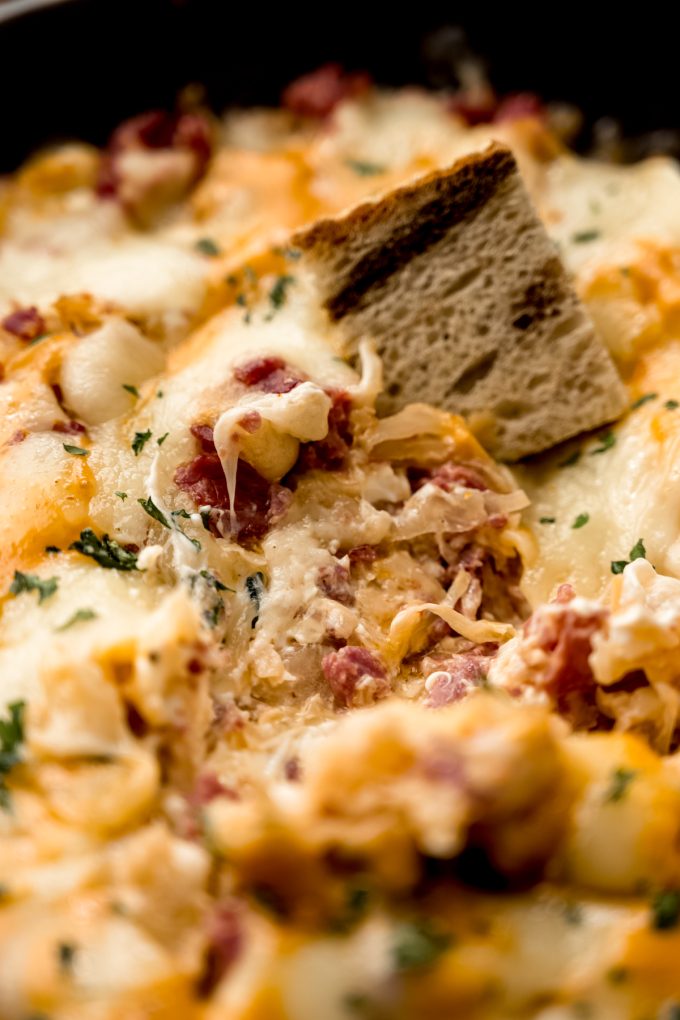 A skillet of Reuben dip with a piece of marbled rye bread in it.