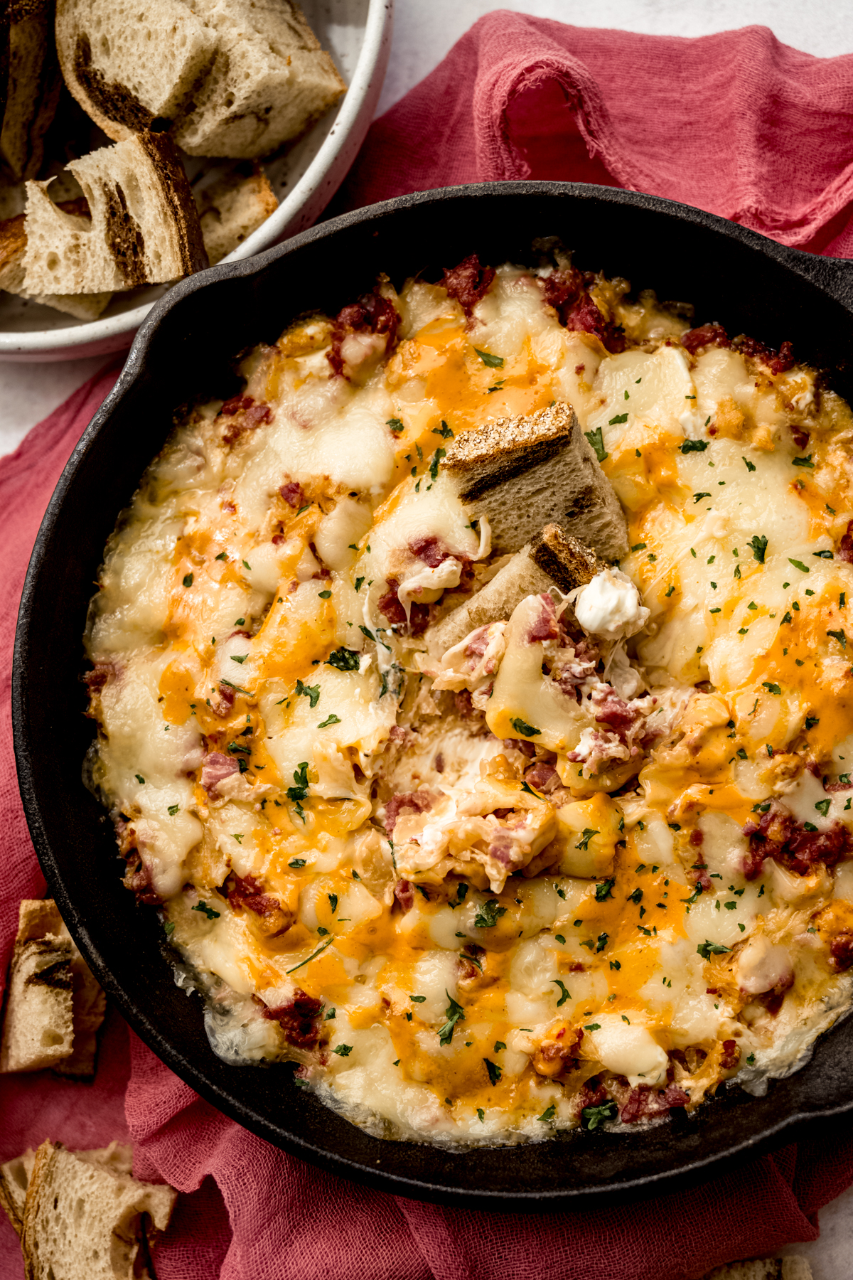 Aerial photo of a skillet of Reuben dip with a piece of marbled rye bread in it.