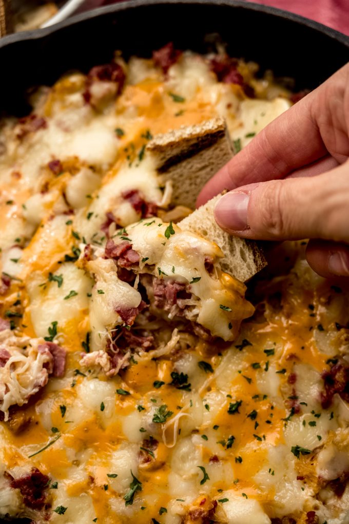 Someone is dipping a piece of marbled rye into hot Reuben dip.