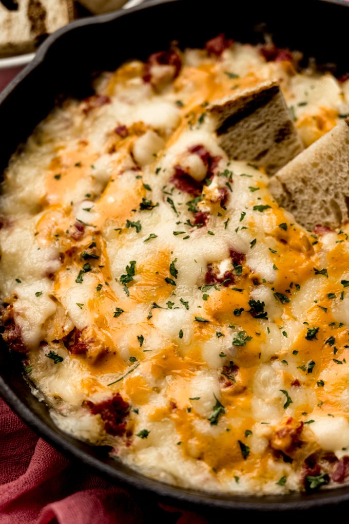 Aerial photo of a skillet of Reuben dip with a piece of marbled rye bread in it.