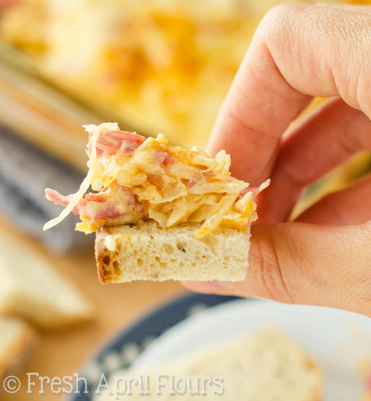 A hand holding a piece of bread with Reuben dip on it.