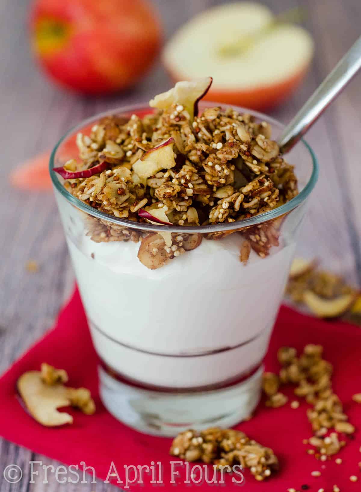 Apple quinoa granola on top of a cup of yogurt with a spoon in it.