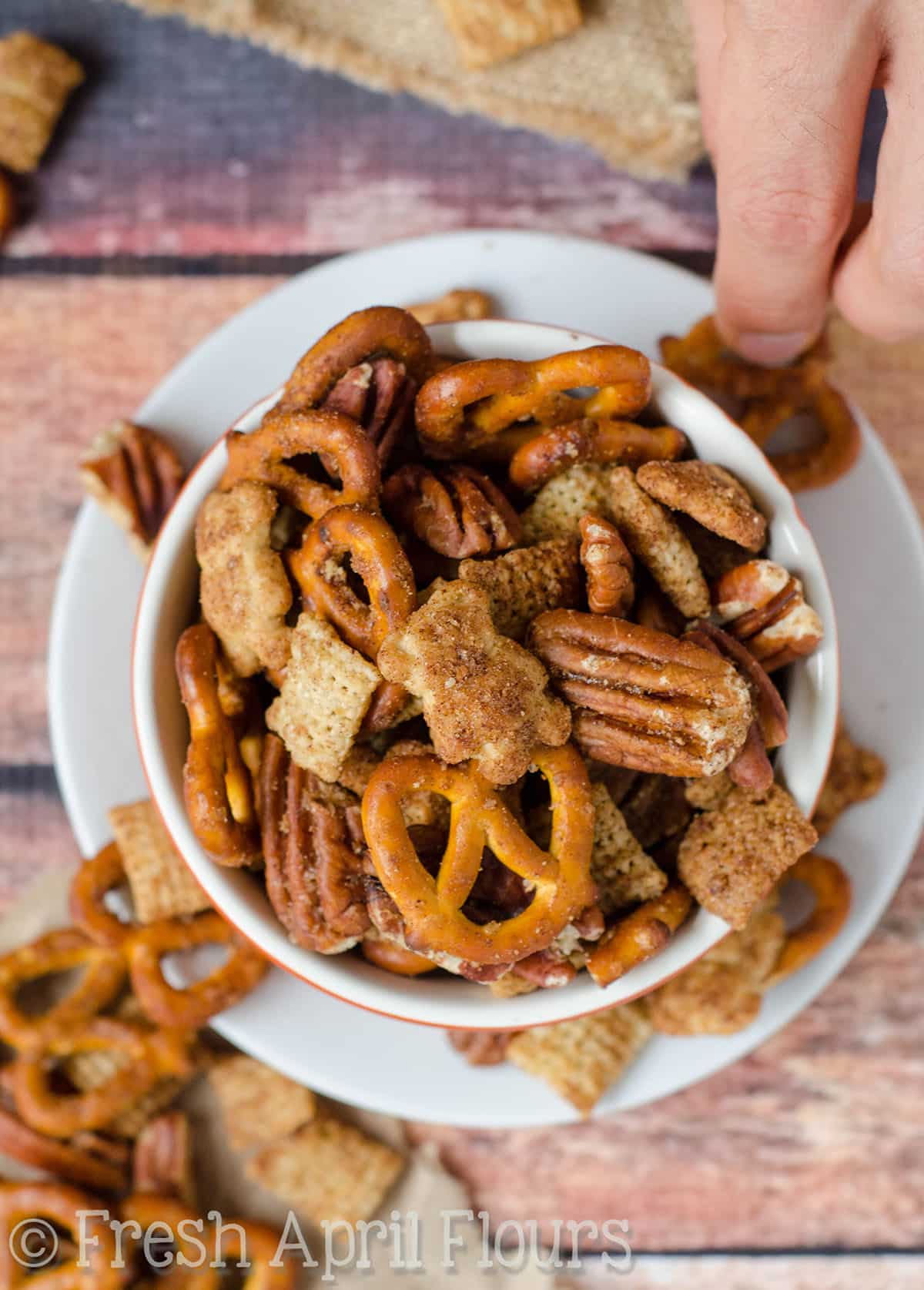 Pumpkin spice chex mix in a bowl and a hand picking up a piece of it.