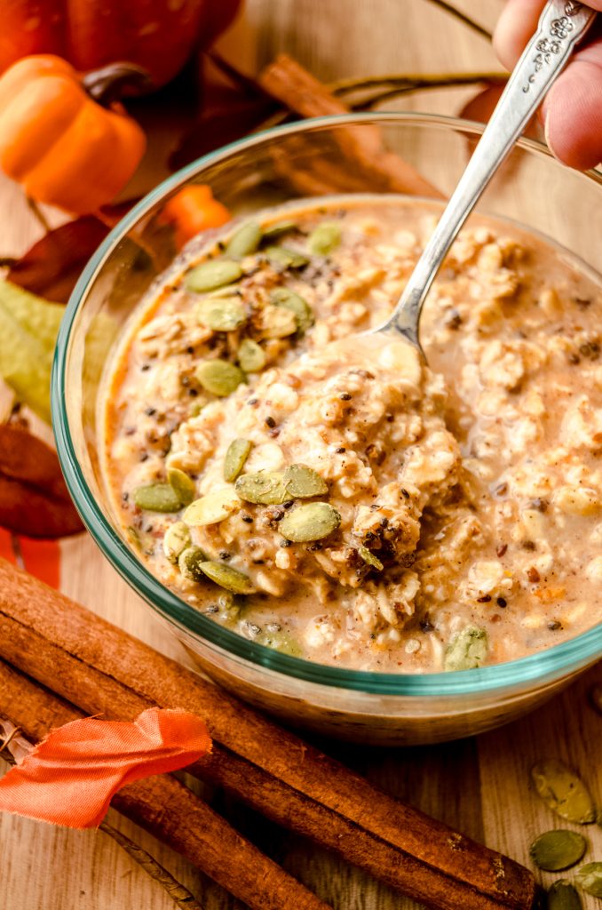 A bowl of pumpkin overnight oats with a spoon in the bowl and pepitas scattered on top.