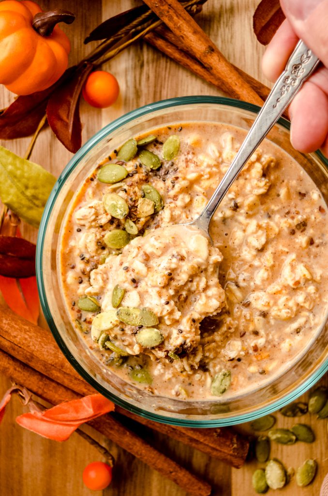 A bowl of pumpkin overnight oats with a spoon in the bowl and pepitas scattered on top.