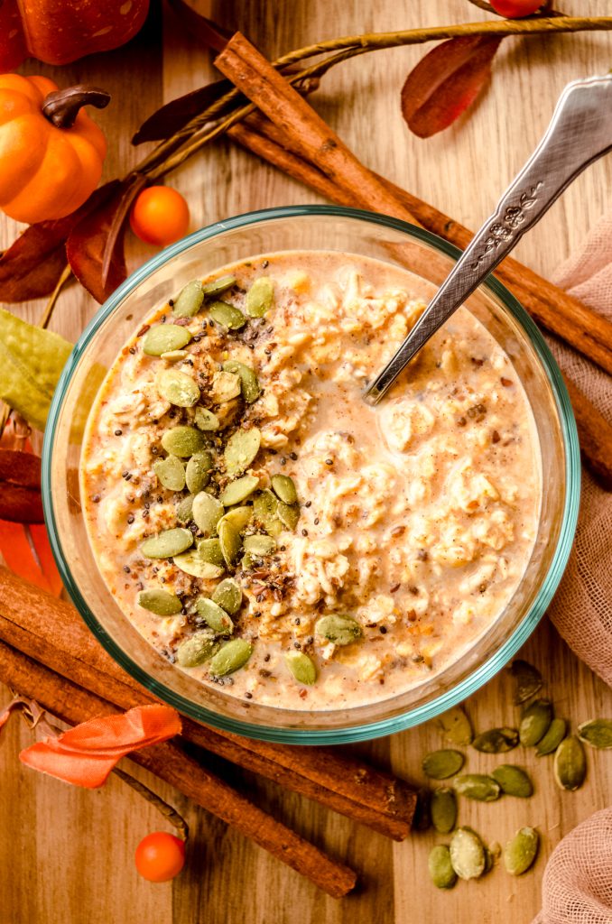 A bowl of pumpkin overnight oats with a spoon in the bowl and pepitas scattered on top.