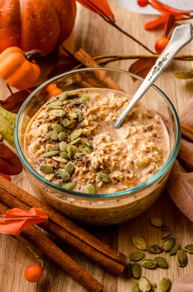 A bowl of pumpkin overnight oats with a spoon in the bowl and pepitas scattered on top.