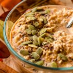 A bowl of pumpkin overnight oats with a spoon in the bowl and pepitas scattered on top.