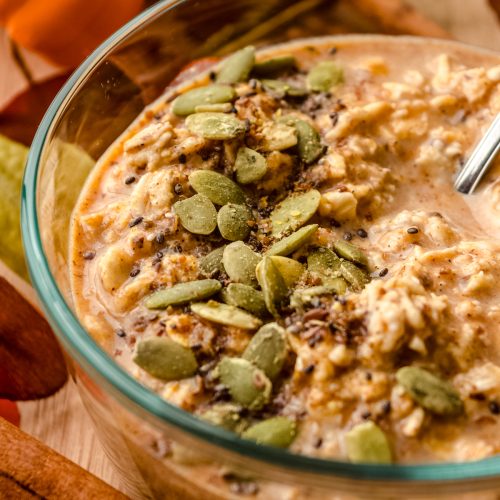 A bowl of pumpkin overnight oats with a spoon in the bowl and pepitas scattered on top.