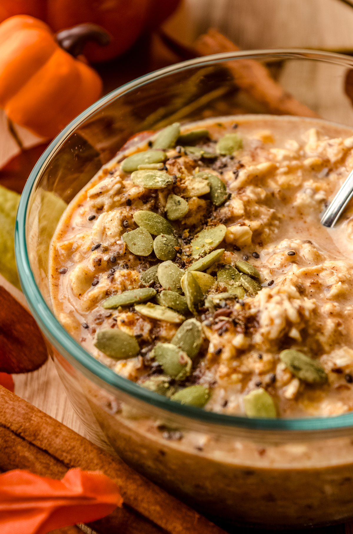 A bowl of pumpkin overnight oats with a spoon in the bowl and pepitas scattered on top.