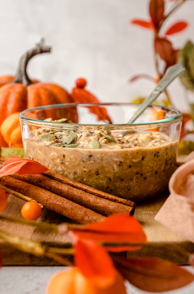 A bowl of pumpkin overnight oats with a spoon in the bowl and fall decor around it.