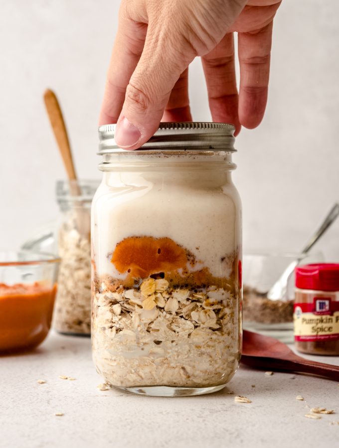 Someone is screwing a lid onto a Mason jar of ingredients to make pumpkin overnight oats.