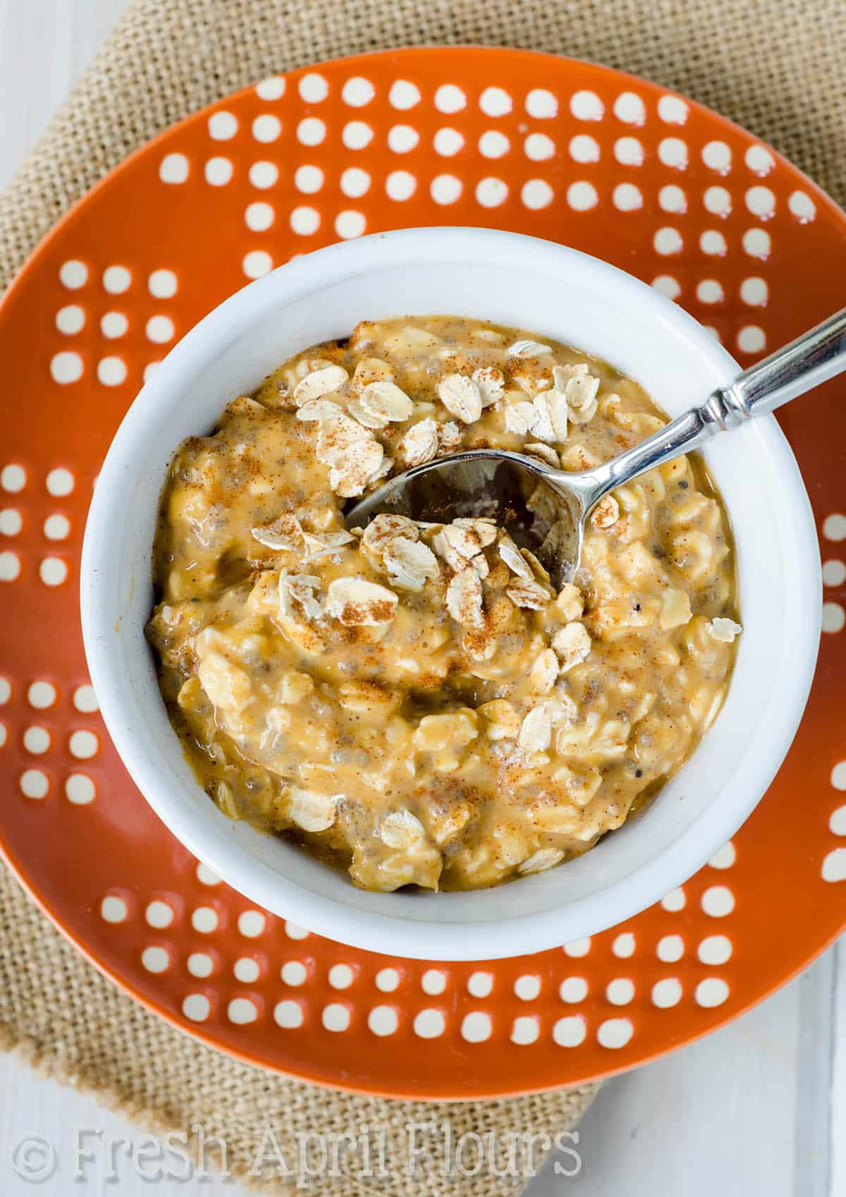 A bowl of pumpkin overnight oats with a spoon in it taking a bite.