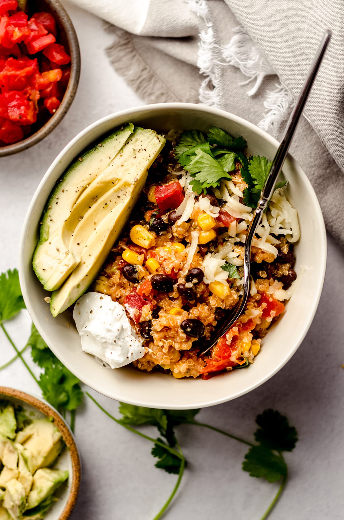 enchilada quinoa casserole in a bowl with sliced avocado, sour cream, and a fork