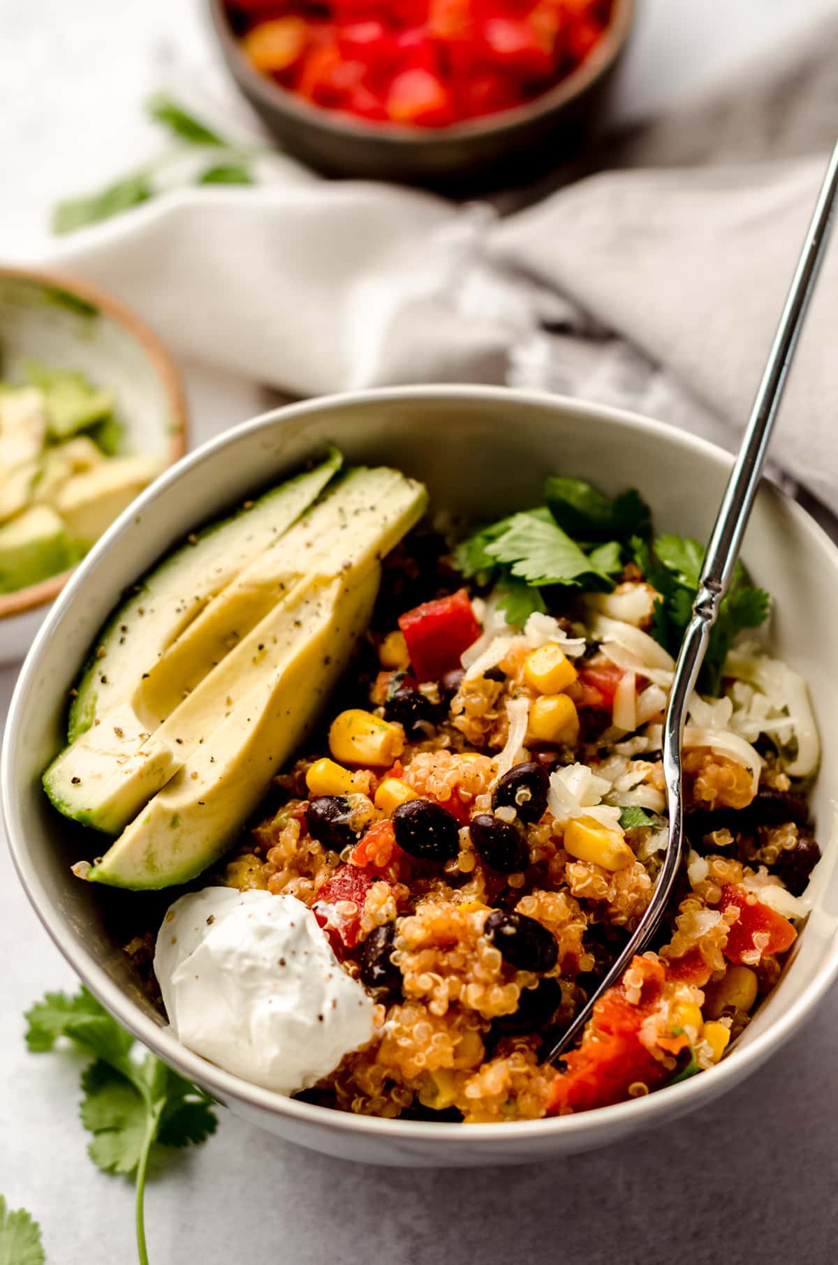 enchilada quinoa casserole in a bowl with sliced avocado, sour cream, and a fork